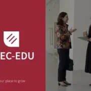 Două femei discutând în holul unei clădiri moderne, cu cafea în mână.